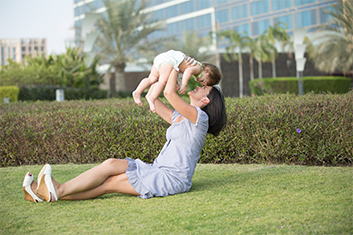 Woman Sitting in Grass Holding Baby in Air with Life Insurance in White Plains